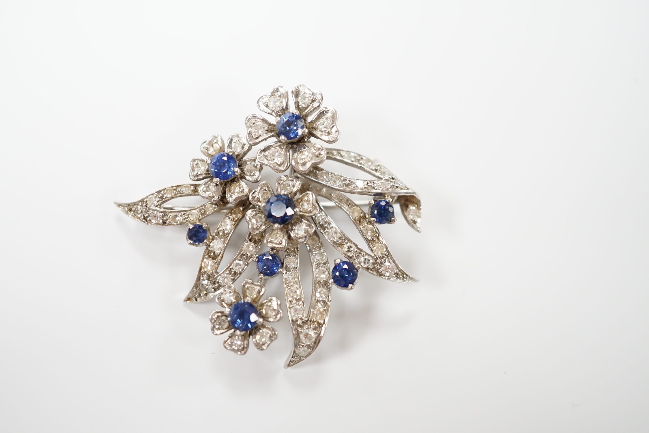 A white metal (stamped 18 plat), sapphire and diamond chip cluster set foliate brooch, 32mm, gross weight 11 grams.